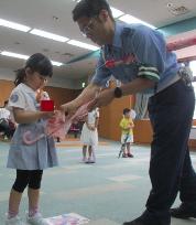 お友だちがおまわりさんに教えてもらいながら、傘を閉じて紐を留める様子です。