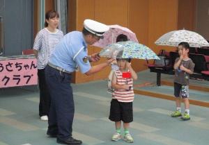 おまわりさんが「雨の日の傘の安全なさしかた」を教えてくれている様子です。